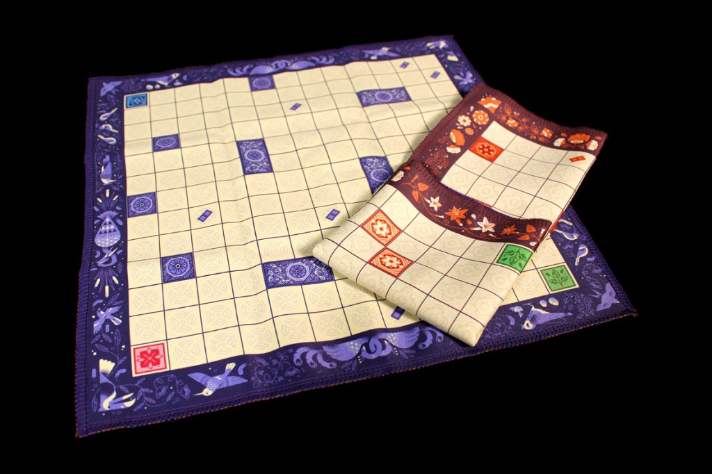 A decorated board game mat featuring a grid layout and colorful border designs, accompanied by a smaller matching cloth piece.