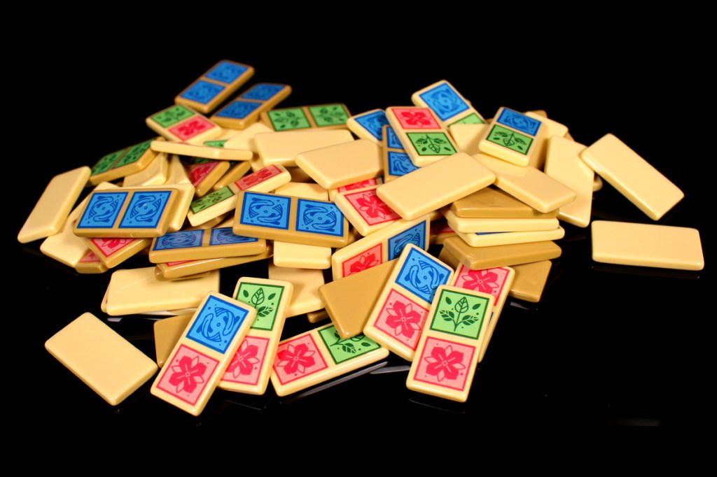 A pile of colorful dominoes featuring blue, green, red, and yellow designs, set against a black background.