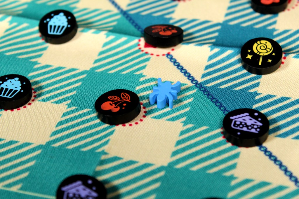 A blue ant figure on a colorful picnic-themed game board surrounded by various food tokens, including cupcakes and candy.