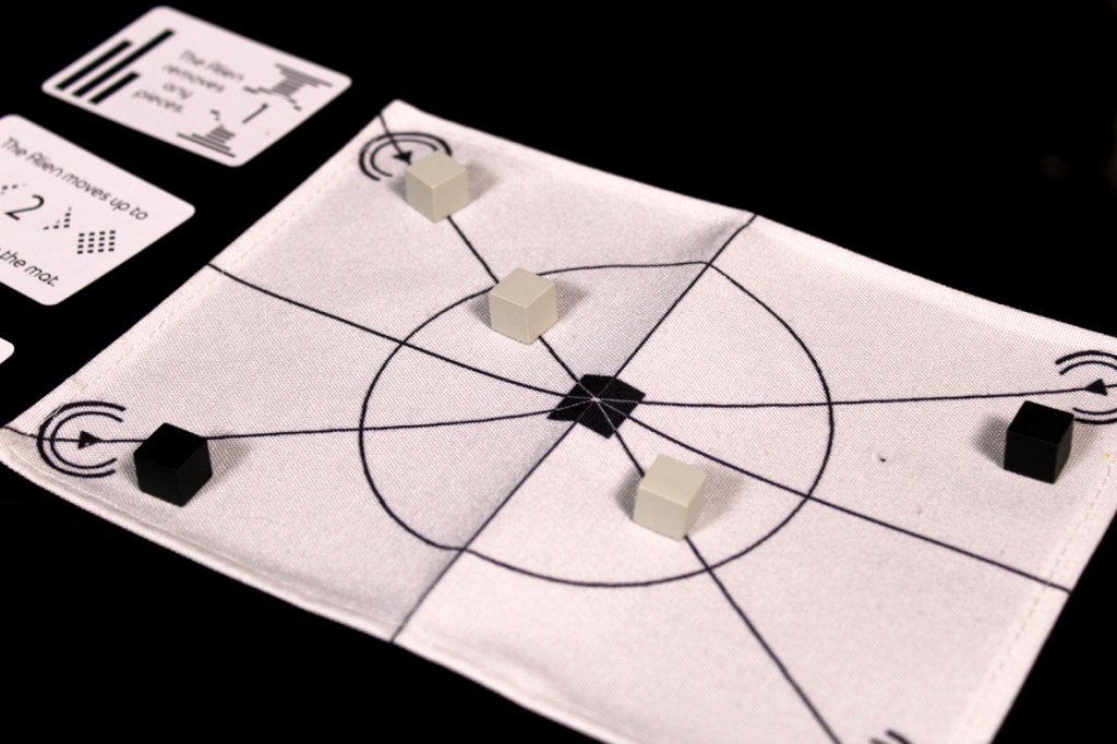 A close-up view of a game board for Signal, featuring a mat with black and white hexagonal tokens positioned on it, along with instruction cards and a grid pattern.