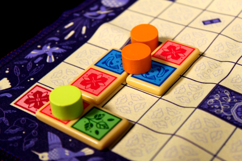 Colorful game board with dominoes and player pieces in yellow, orange, and green, showcasing a strategic placement during gameplay.
