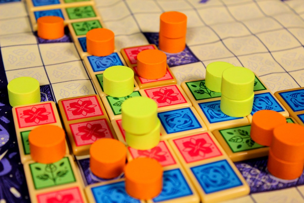 A close-up view of a board game setup featuring various colored domino tiles and player tokens on a grid surface.