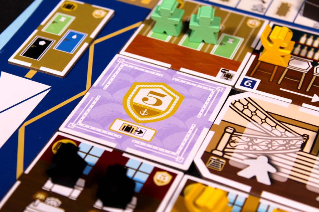 Close-up of a board game showing various colored tiles and game pieces on a ship layout, highlighting numbered room tiles and player tokens.