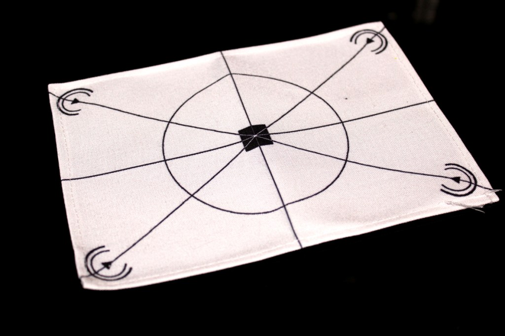 A white mat with a circular design and intersecting lines, featuring symbols at the corners.