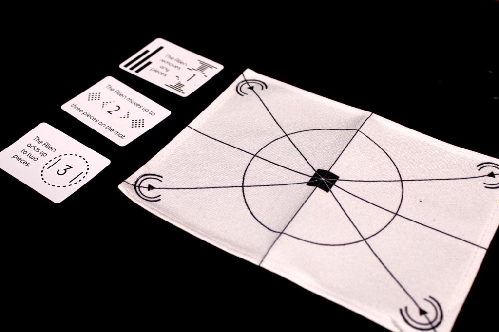 A game setup featuring an Alien movement mat and three action cards with instructions in a black-and-white design.