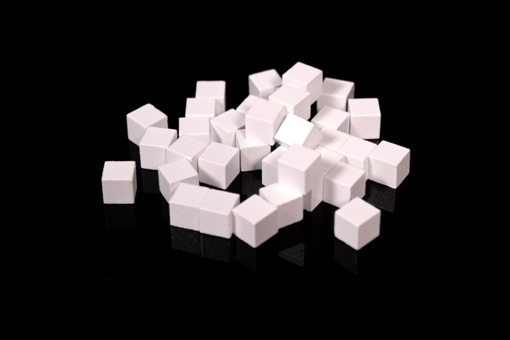 A close-up image of multiple white sugar cube tokens arranged on a black surface.