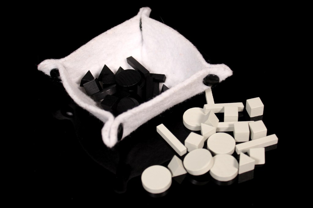 A small felt container holds various black and white geometric game pieces, including circles, squares, and triangles, against a black background.