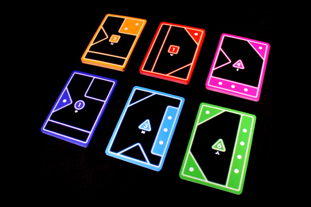 A colorful assortment of six playing cards in vibrant neon colors, including orange, red, blue, green, and pink, displayed against a black background.
