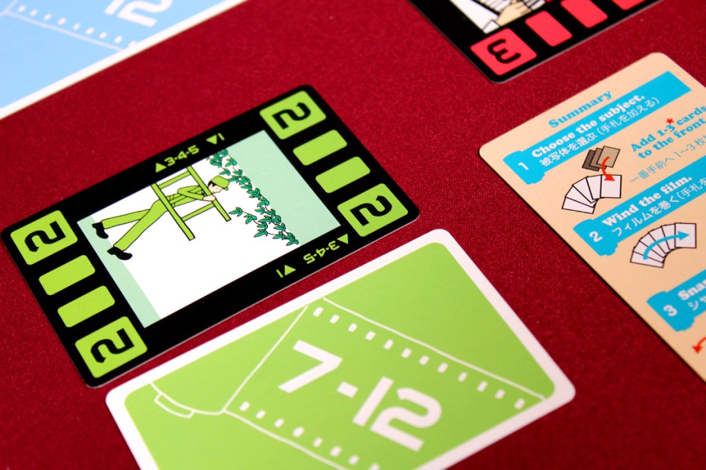 Close-up of a board game setup featuring a filmstrip card depicting a character in an olive green outfit next to summary instructions for gameplay.