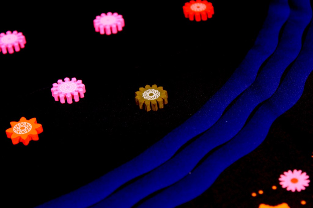 Colorful wooden flower tokens scattered on a dark surface, with blue fabric accents.