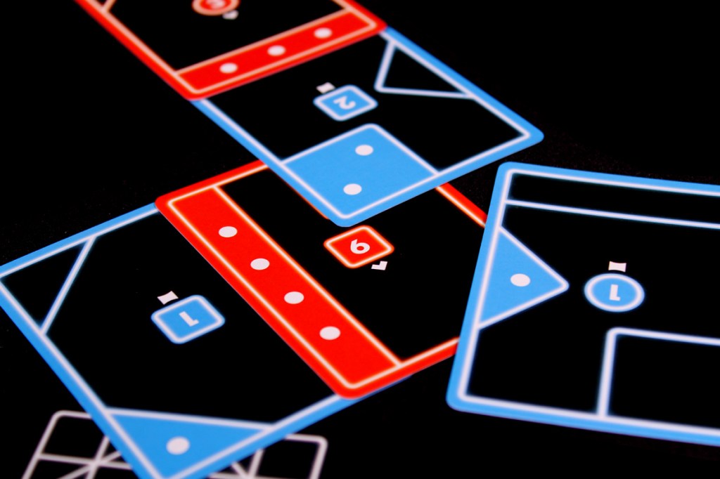 Colorful game cards in blue and red arranged on a black surface, featuring shapes and numbers for gameplay.