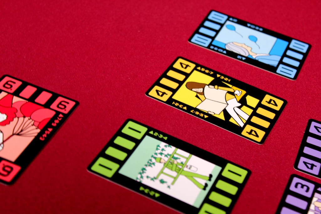 A close-up of various colorful filmstrip cards laid out on a red surface, depicting different illustrations and numbers.