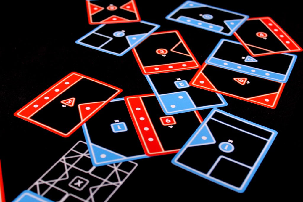 Array of game cards in red and blue colors laid out on a black background, displaying various shapes and numbers.