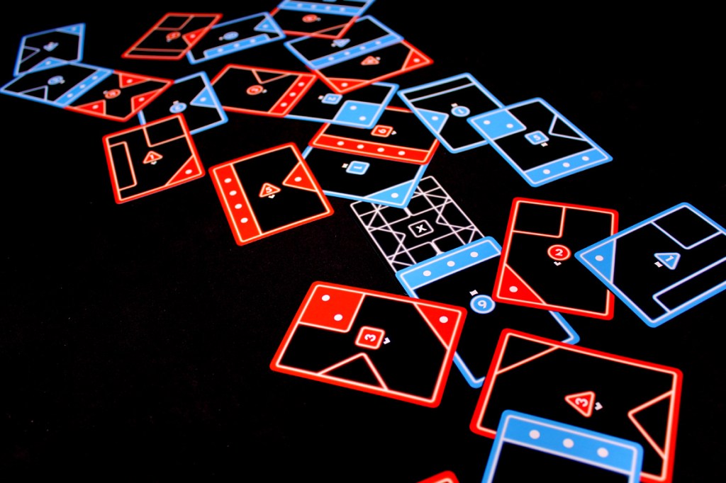 A scattered display of blue and red game cards on a black background, showcasing various shapes and numbers that represent a board game setup.