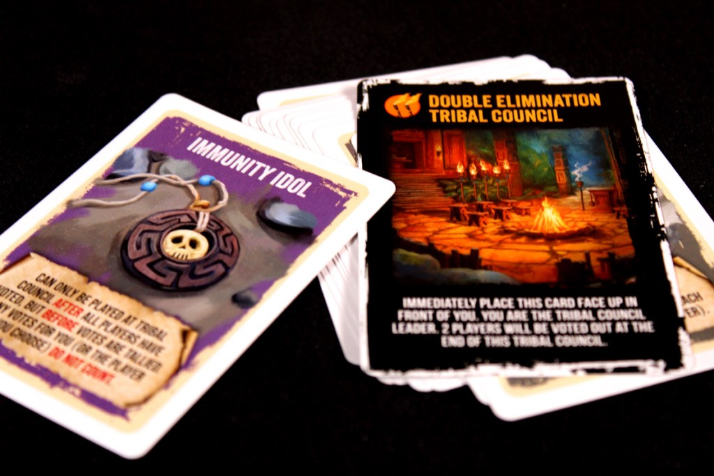Close-up of two game cards from Survivor: The Tribe Has Spoken, featuring the Immunity Idol card and the Double Elimination Tribal Council card.
