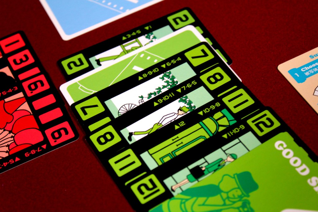 A close-up view of colorful game cards from the board game 'Wind the Film,' featuring illustrations and numbers on a red surface.