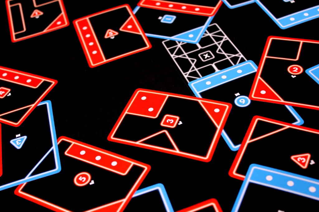 A close-up view of colorful playing cards in red and blue, featuring geometric designs and numbers, laid out on a black surface.