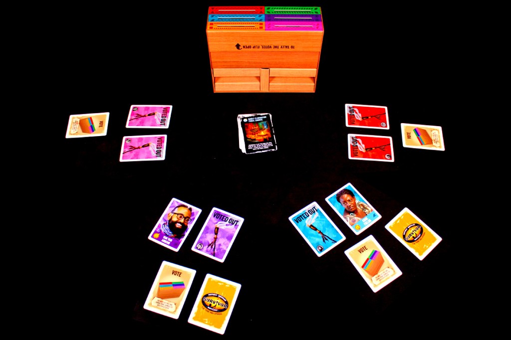 A board game setup featuring various colored vote cards arranged around a central voting box, with two cards indicating 'Voted Out' and character representations.