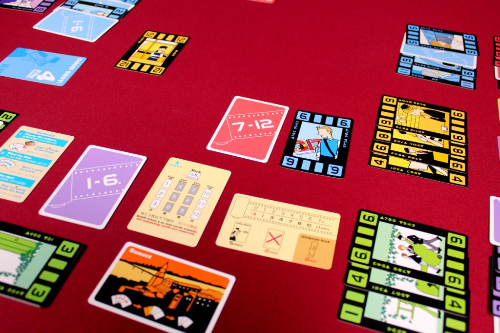 A tabletop view of various colorful cards laid out on a red surface, featuring numbers and illustrations related to gameplay.