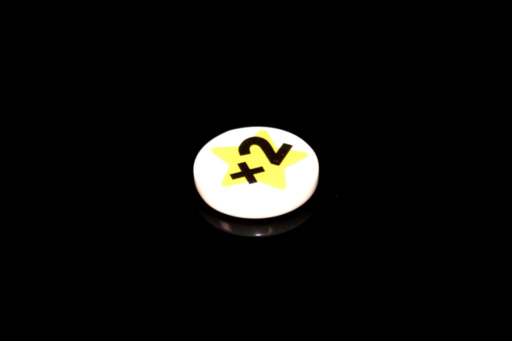 A round gaming token featuring a yellow star and a '+2' symbol, displayed on a black background.