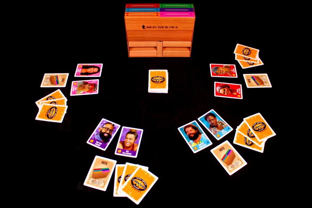 Game setup for Survivor: The Tribe Has Spoken, displaying character and vote cards arranged around a central deck within a wooden box.