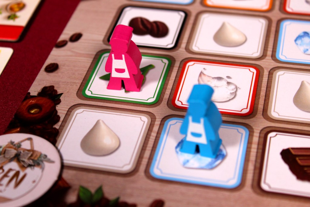 Two colored meeples on a game board with various ingredient tiles, depicting a coffee shop theme.