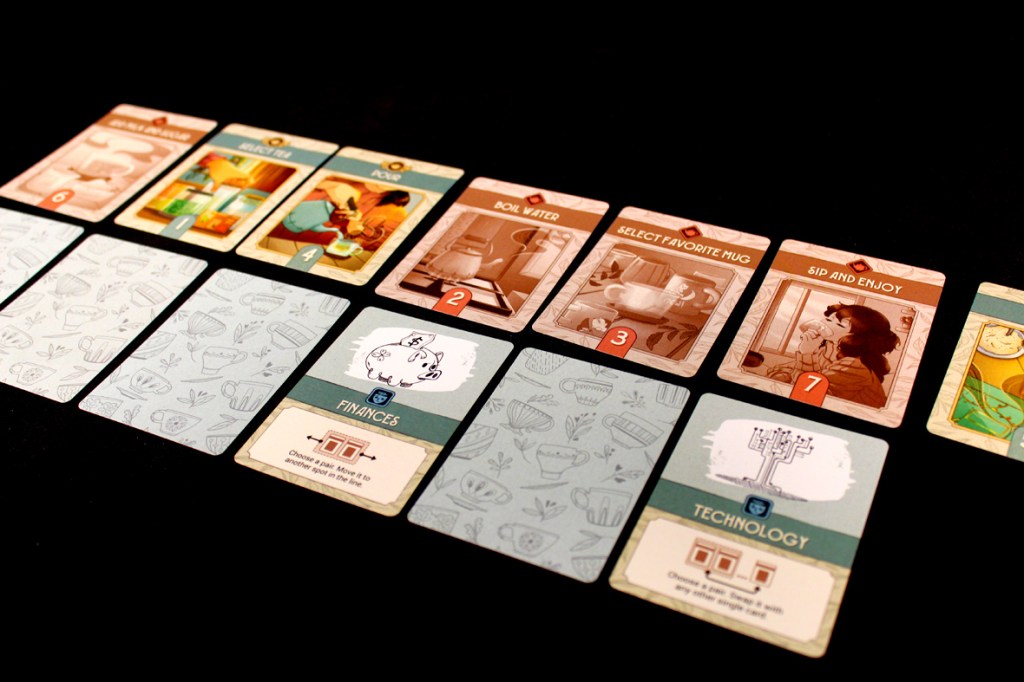 A game board featuring various colorful tea-related cards laid out in a row, alongside several face-down Worry Cards and two special cards labeled 'Finances' and 'Technology'.