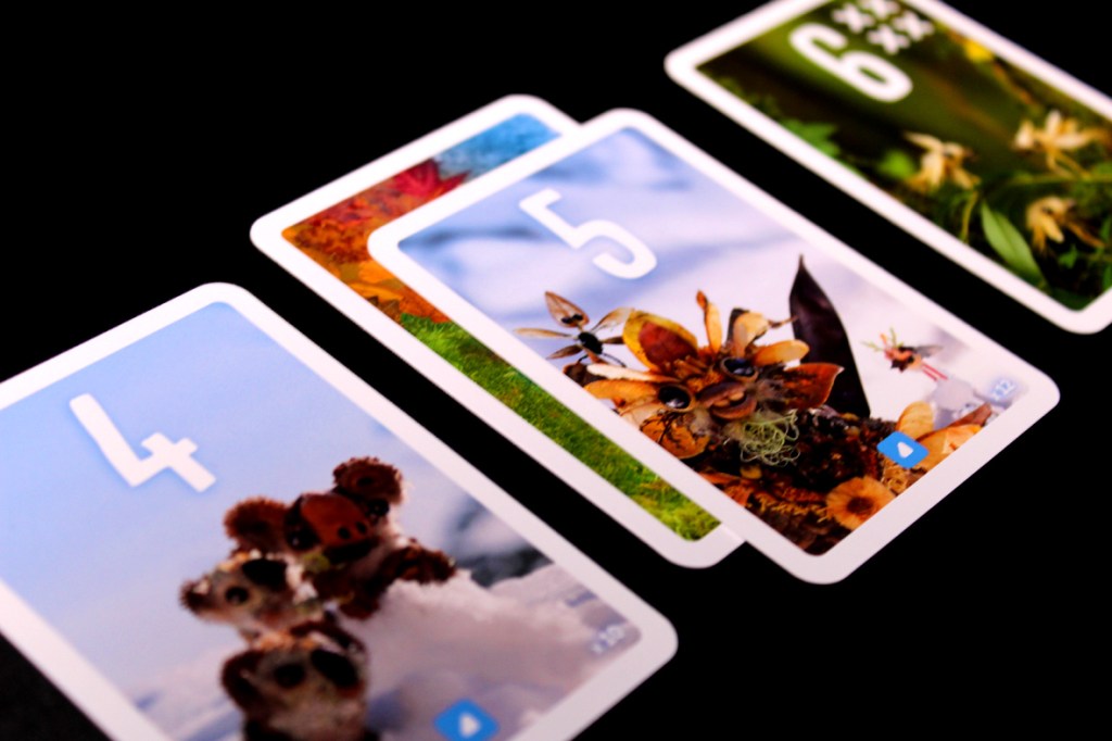 A close-up of four playing cards from the game Pixies, featuring various colorful designs and the numbers 4, 5, and 6 prominently displayed.