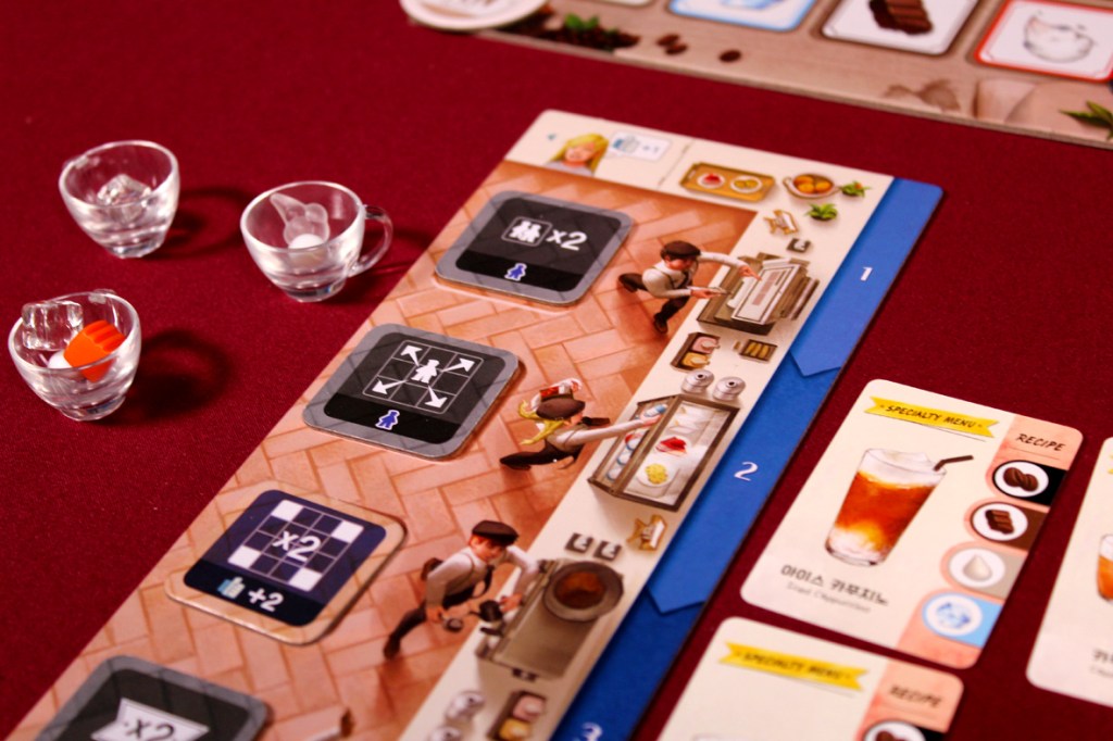 Close-up of a player board from the game Coffee Rush, featuring cups, upgrade tiles, and order cards, arranged on a maroon table.