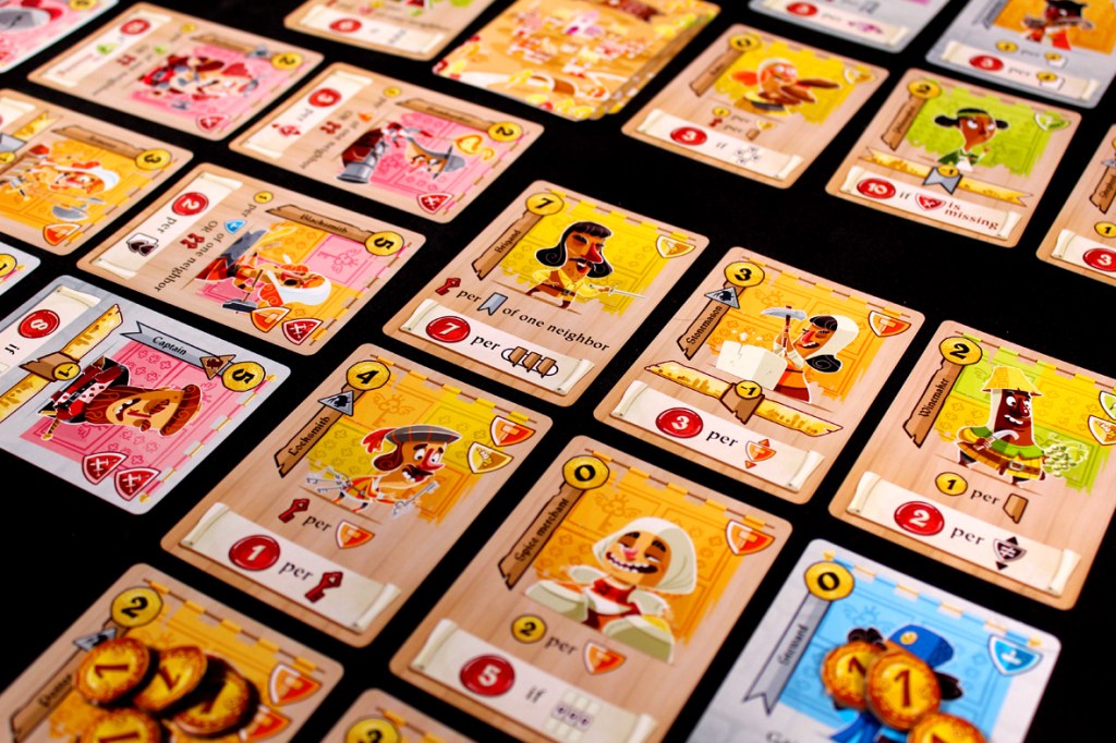 A colorful assortment of cards laid out on a table, featuring whimsical illustrations and various game symbols. The cards display different characters and abilities, highlighting their unique powers and point values.