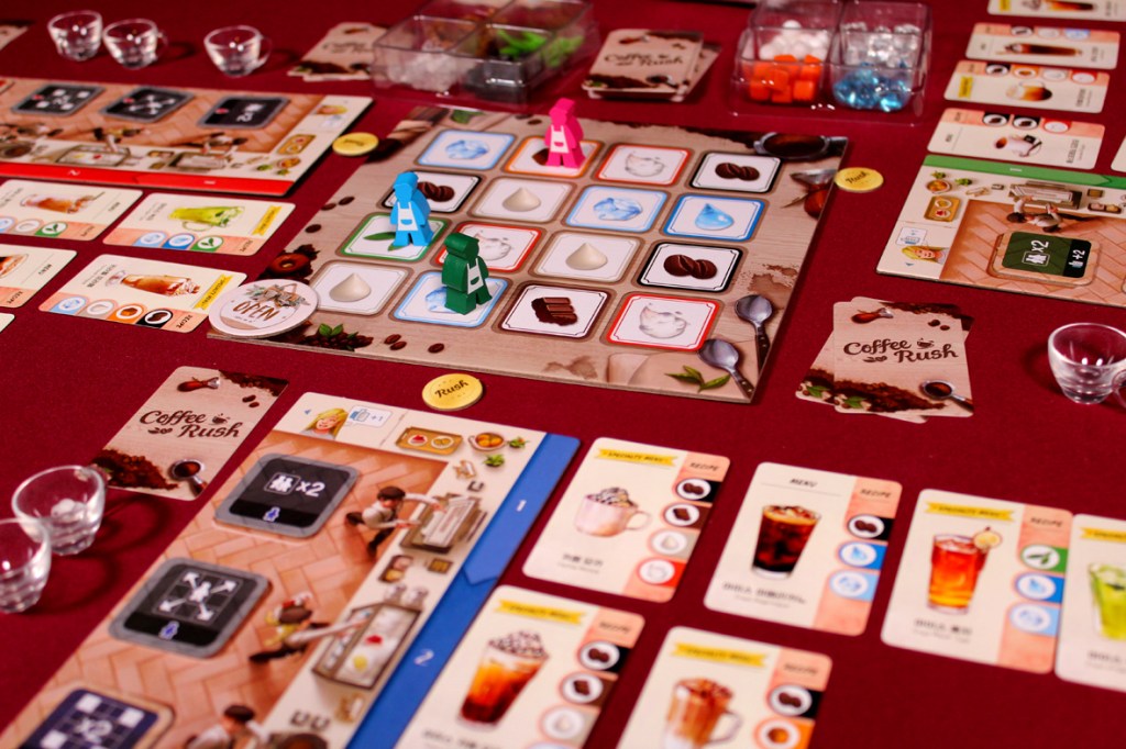 Board game setup for Coffee Rush, displaying colorful player pieces, ingredient tokens, and recipe cards on a maroon table.
