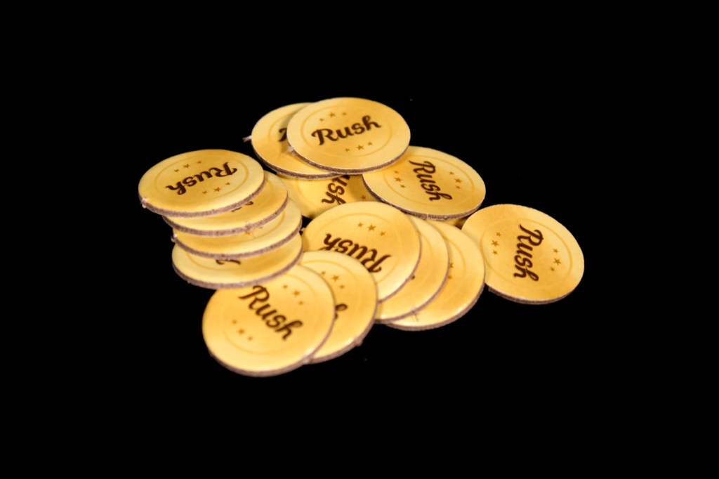 A stack of wooden tokens labeled 'Rush' scattered on a black background.