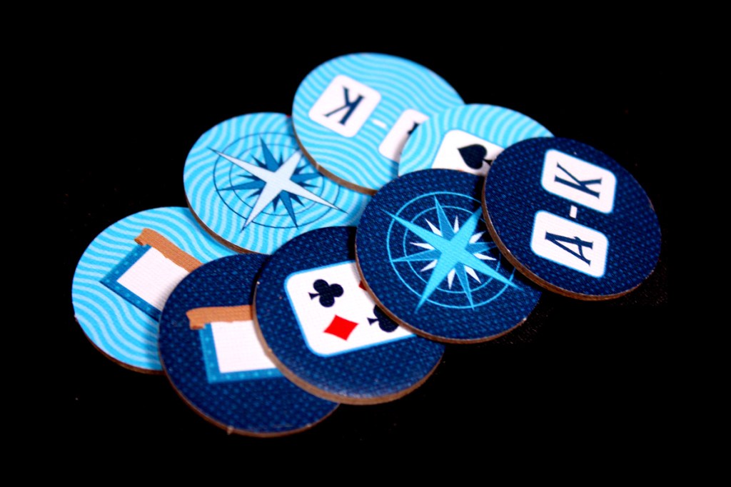 A collection of game tokens featuring nautical-themed designs, including compasses and playing card symbols, arranged on a black background.