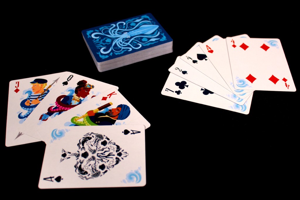 A set of playing cards featuring nautical-themed illustrations, including a deck and several face cards showcasing characters in an underwater setting. The cards are laid out on a black background.
