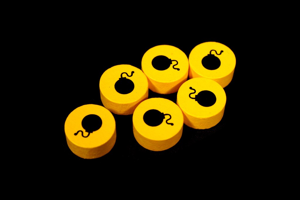 Six yellow game pieces designed to resemble bombs, featuring a black bomb icon on each piece, set against a black background.