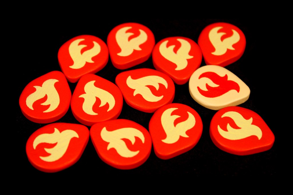 A collection of red and white flame tokens used in the board game Fuego, arranged on a black background.