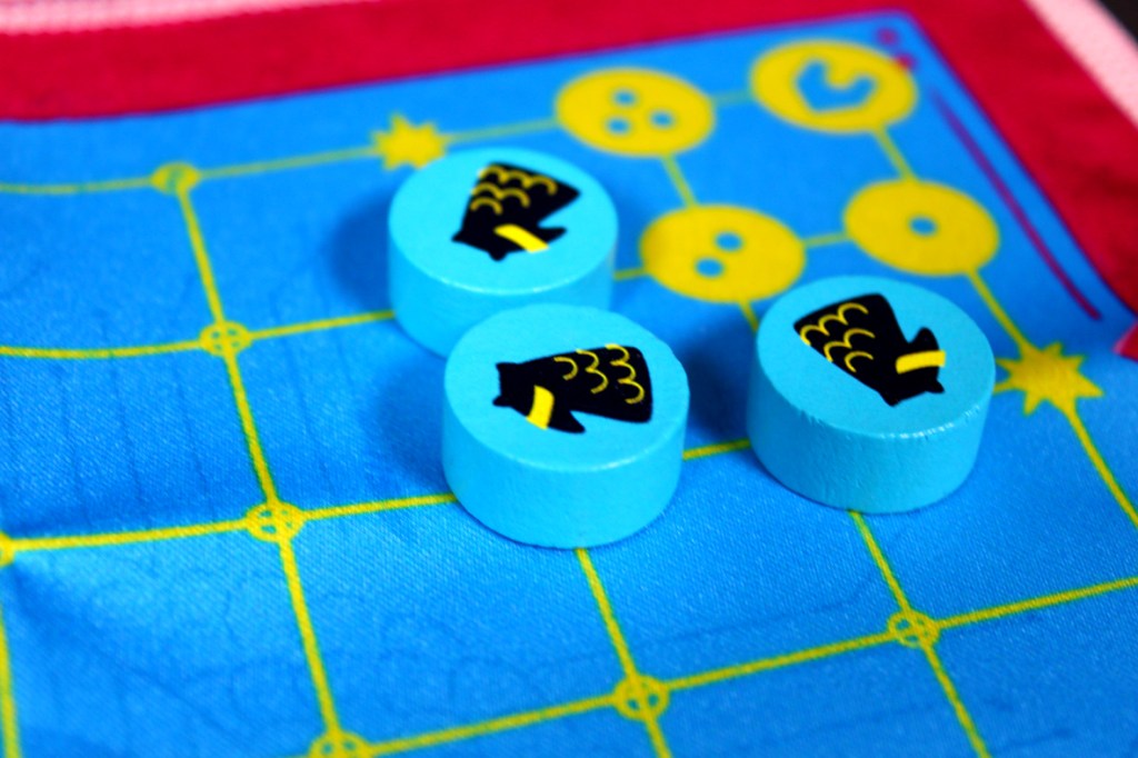 Three blue game pieces with black designs on a colorful game board featuring a grid pattern.