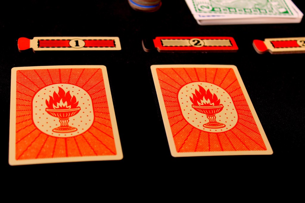 Two red Flame Tokens from the game Fuego displayed on a black background, with a number one token beside them.