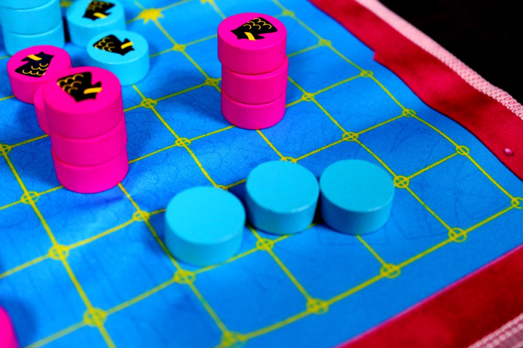 Close-up of a colorful game board featuring stacked pink and blue tokens on a blue grid with yellow lines.