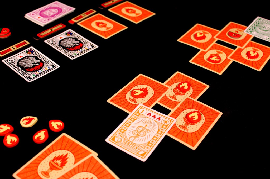An overhead view of a tabletop game setup featuring colorful cards and flame tokens, showcasing gameplay elements for the game 'Fuego'.