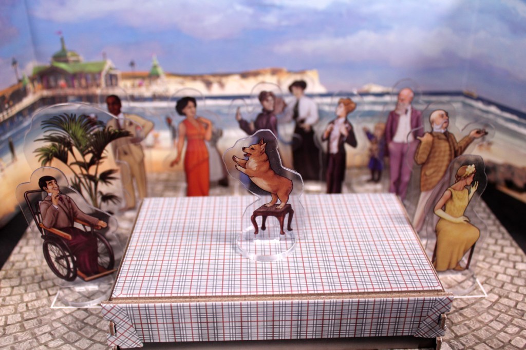 A colorful board game setup with various character cutouts, including a dog on a stool, in front of a beach backdrop.