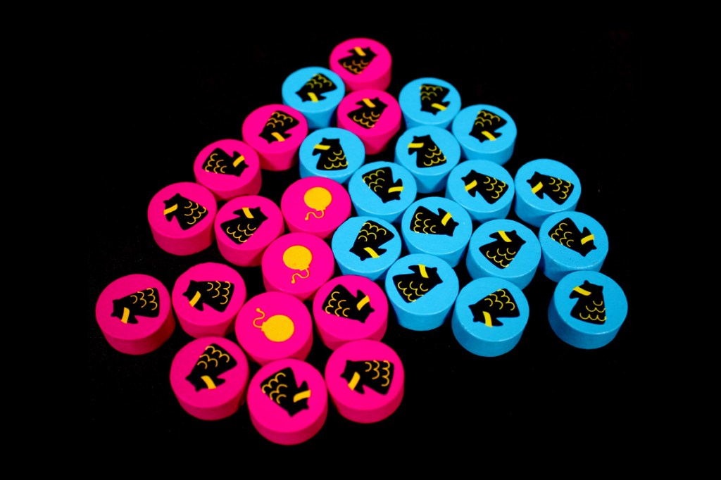 Colorful game pieces including pink and blue tokens with various designs, displayed on a black background.