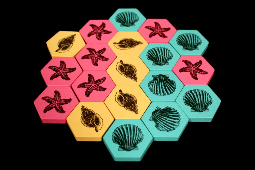 A colorful arrangement of hexagonal game tiles featuring starfish and seashell designs in pink, yellow, and teal colors.