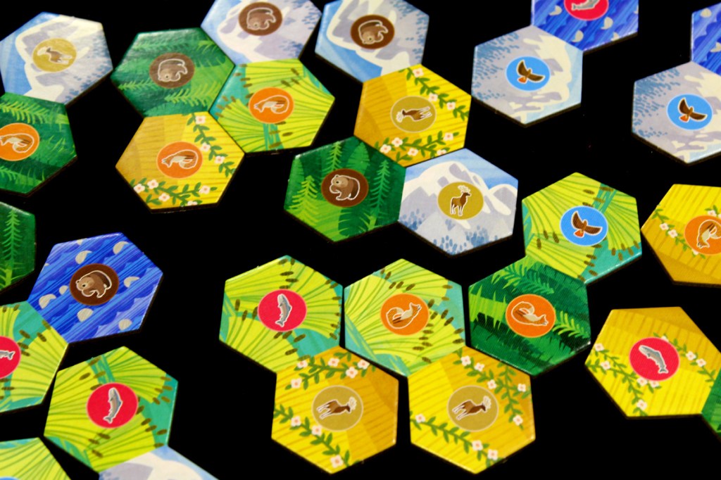 A close-up view of hexagonal game tiles featuring various animals and landscape designs, used in the board game Cascadia Junior.