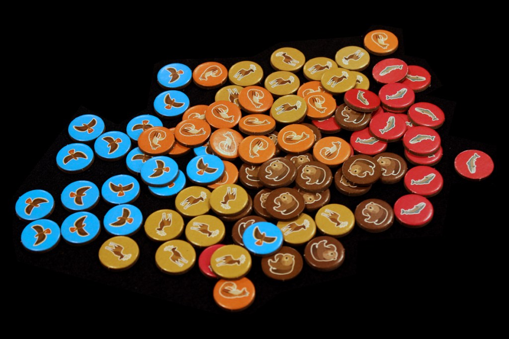 A collection of round tokens featuring various animal illustrations, including fish, bears, and birds, in multiple colors arranged on a dark background.