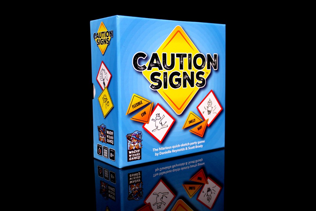 A brightly colored box of the party game 'Caution Signs,' featuring a yellow diamond logo and various cartoon signs depicting humorous themes, reflecting its quick-sketch gameplay.