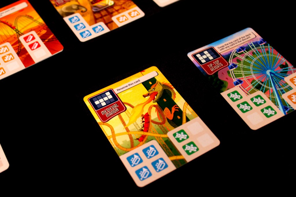Close-up of multiple park cards from the game Lands of Amazement, showcasing vibrant artwork and various icons for gameplay mechanics on a black background.