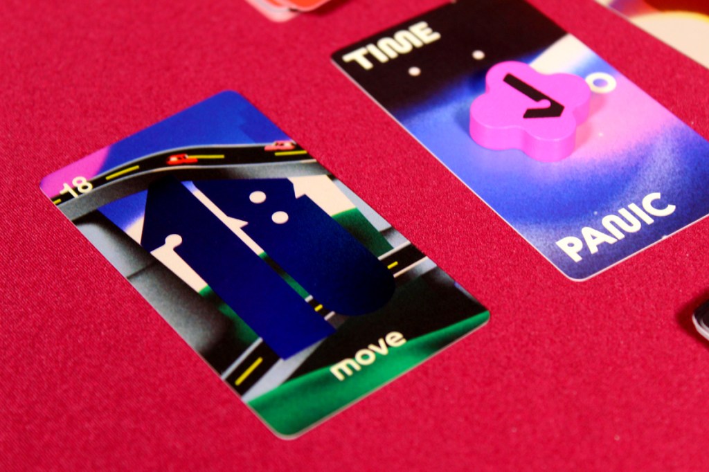 A close-up of a game card from a board game, showing a large number '18' and an illustration of a road with cars, alongside a pink token labeled 'PANIC' and a card indicating 'TIME'.