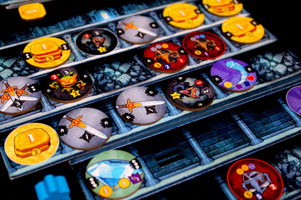 Close-up view of game pieces from Satchel Quest, including gold tokens, skill chips, and monster cards arranged on a market board.