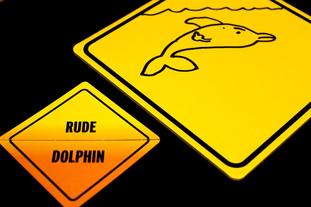 A yellow caution sign depicting a dolphin jumping out of water, alongside a card that reads 'RUDE DOLPHIN'.